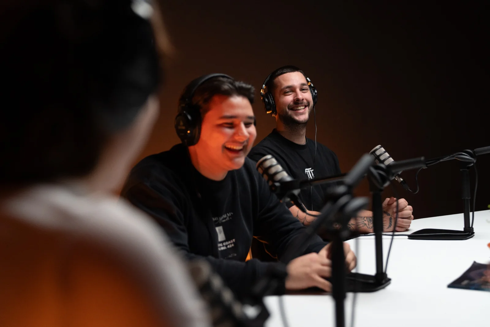 Twee mannen lachend aan tafel in een podcast studio