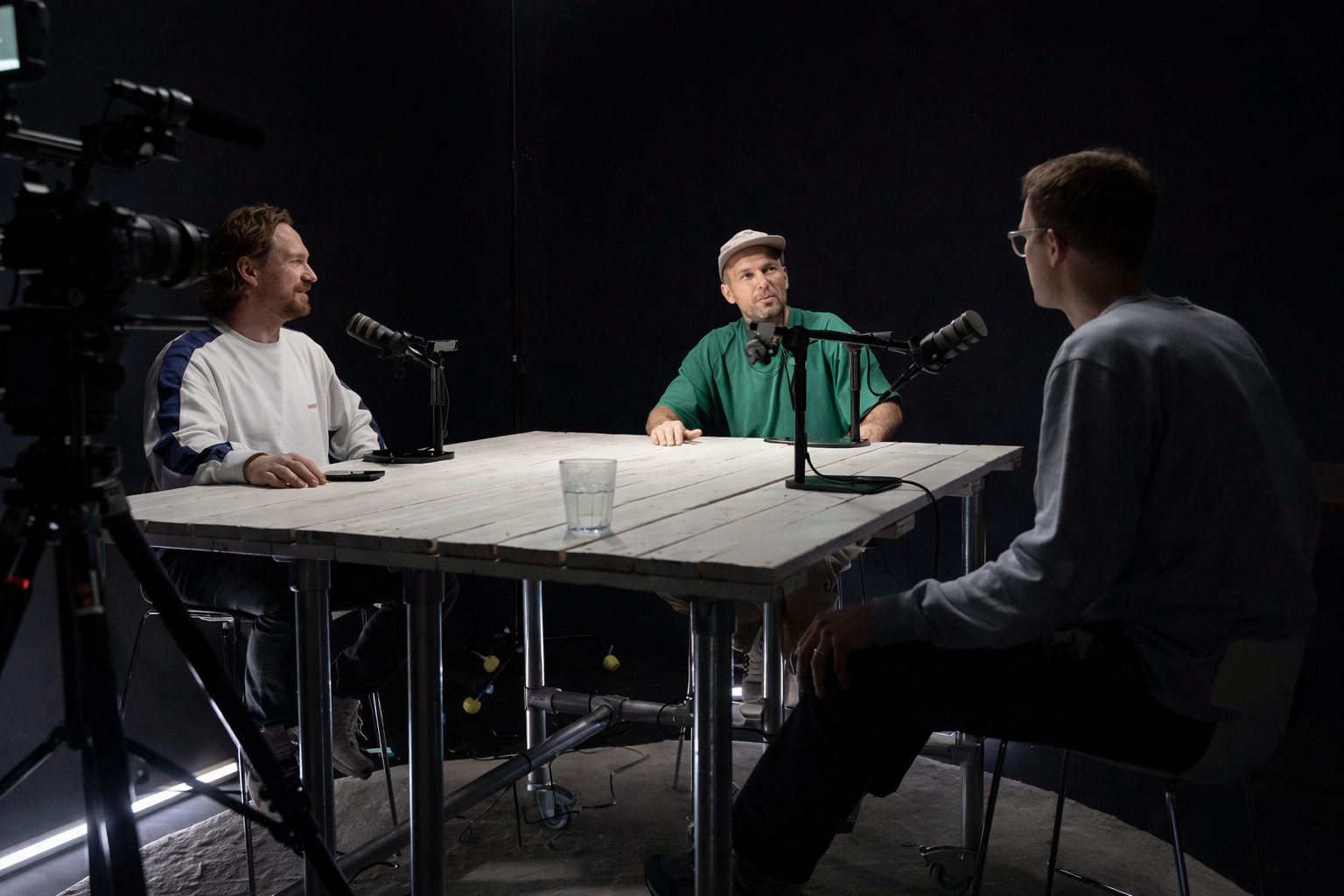 Twee podcasters nemen een aflevering op in een professionele podcaststudio met microfoons en camera-opstelling.